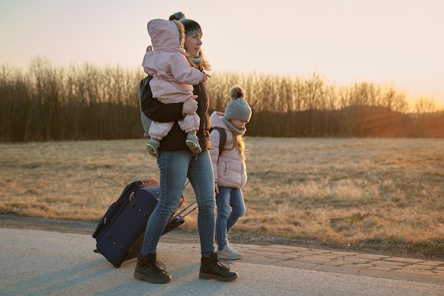 Foto madre e hija caminan por la carretera y llevan maletas sobre ruedas refugiados