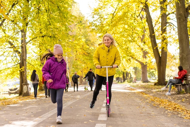 Madre e hija caminan en otoño en el parque. mujer está montando un scooter