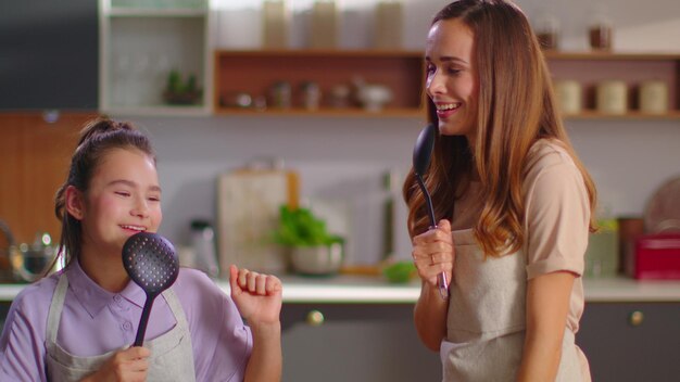 Madre e hija cantando en cuchara en la cocina Familia divirtiéndose en casa