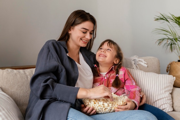 Foto madre e hija en casa comiendo palomitas de maíz