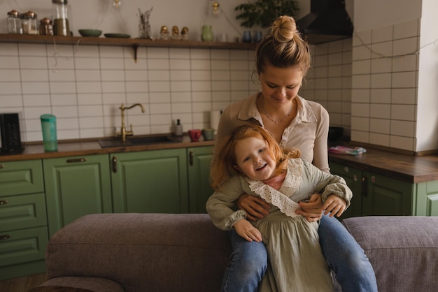 Madre e hija caucásicas alegres de 23 años vestidas de casa juegan entre sí en el interior Concepto de estilo de vida familiar