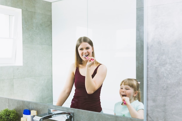 Foto madre e hija cepillarse los dientes cerca del espejo