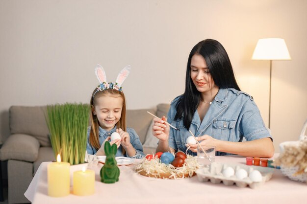 Madre e hija en una cocina moderna y ligera y pintando juntos los huevos de Pascua