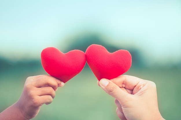 Madre e hija con corazón rojo juntos en el fondo de la naturaleza