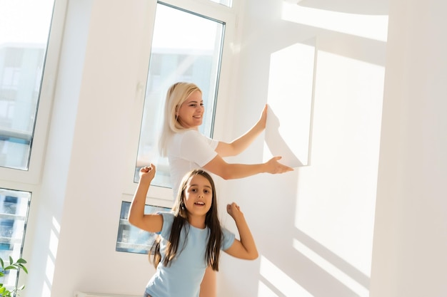 madre e hija cuelgan un gran lienzo fotográfico en casa