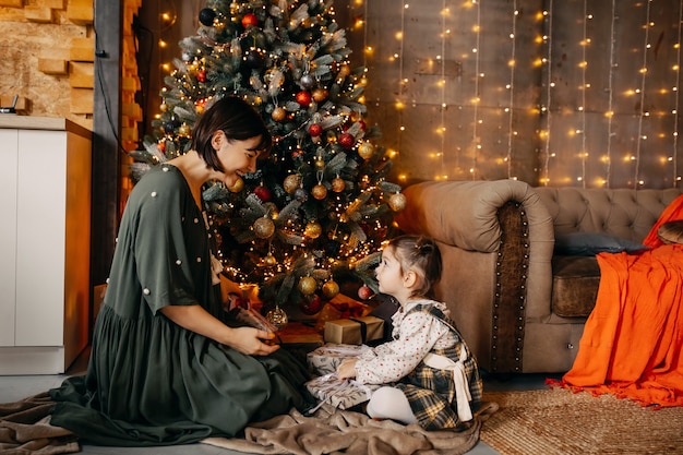 Madre e hija dándose regalos, sentados junto a un árbol de Navidad