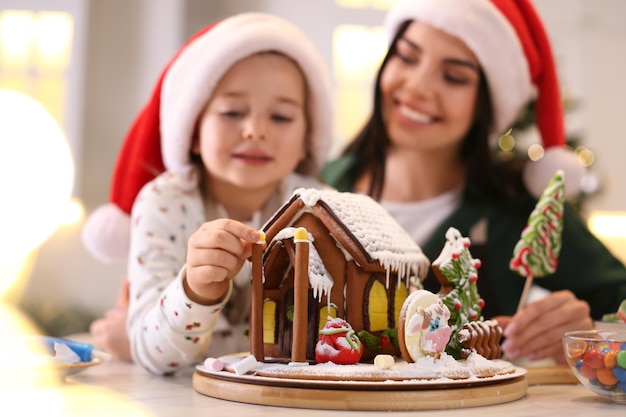 Madre e hija decorando la casa de pan de jengibre en la mesa en el interior