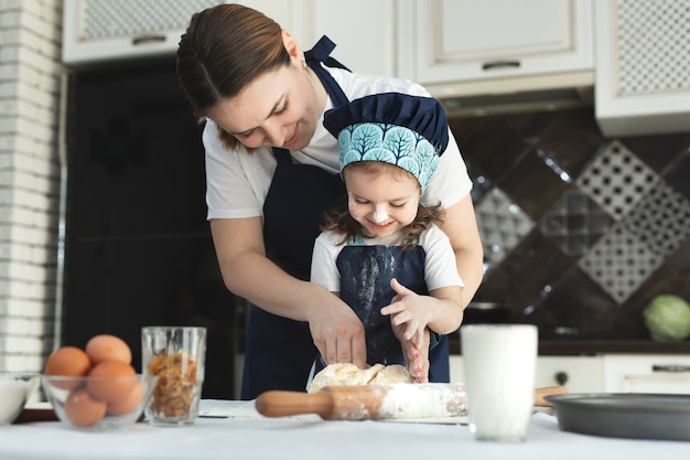 Madre e hija en delantales a juego y gorro de cocinero cocinando en la cocina