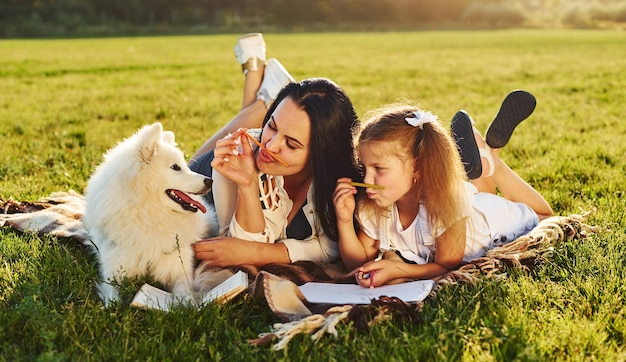 Madre e hija descansan mientras se acuestan en el césped con su lindo perro