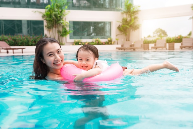 Madre e hija divirtiéndose en la piscina. Vacaciones de verano y concepto de vacaciones.