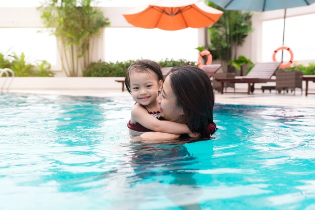 Madre e hija divirtiéndose en la piscina. Vacaciones de verano y concepto de vacaciones.