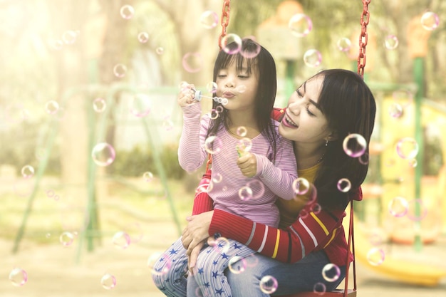 Madre e hija divirtiéndose con pompas de jabón en el patio de juegos Concepto de verano o primavera