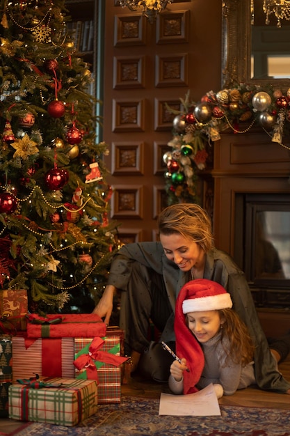 Madre e hija escribiendo una carta a Santa Claus en el salón decorado de Navidad