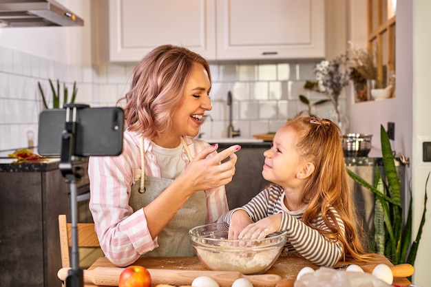 Madre e hija están amasando masa y sonriendo mientras la preparan para hornear, en una cocina ligera en casa