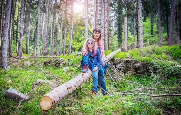 Madre e hija están sentadas en el tronco del árbol en el bosque