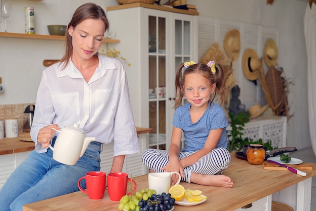 madre e hija de familia feliz están bebiendo té en la cocina desayuno familiar