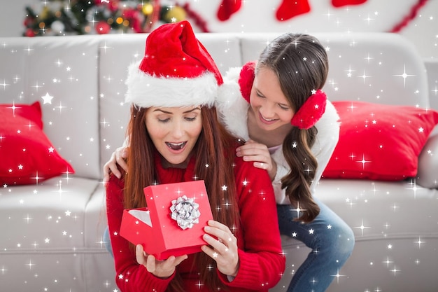 Madre e hija festivas con un regalo de navidad contra estrellas centelleantes