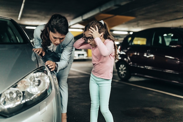 Madre e hija frustradas y aterrorizadas mirando su coche rayado.