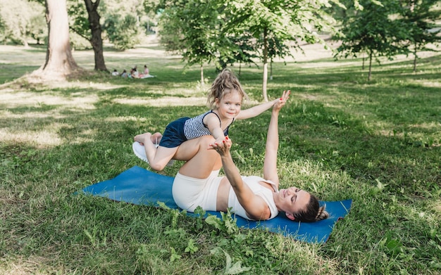 Madre e hija hacen ejercicios de yoga en el césped del parque durante el día estilo de vida saludable