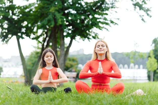 Madre e hija haciendo ejercicios de yoga sobre el césped en el parque durante el día