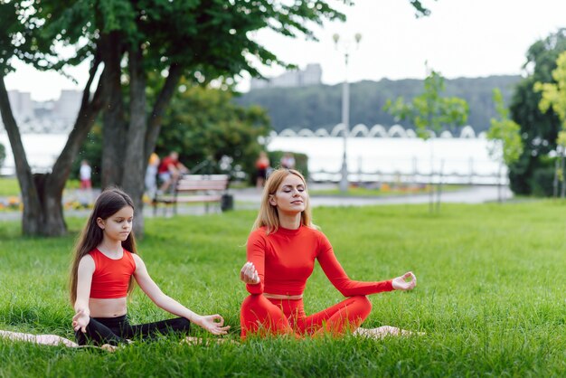 Madre e hija haciendo ejercicios de yoga sobre el césped en el parque durante el día