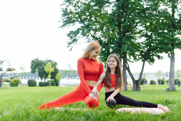 Madre e hija haciendo ejercicios de yoga sobre el césped en el parque durante el día