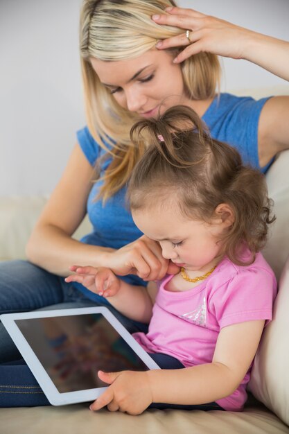 Foto madre e hija joven que usa la tableta digital en el sofá en casa