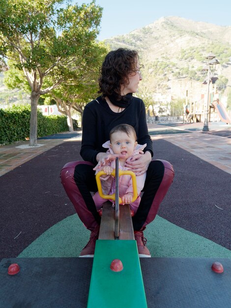 Madre e hija jugando en el balancín del parque.
