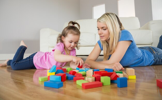 Madre e hija jugando con bloques de construcción en el piso