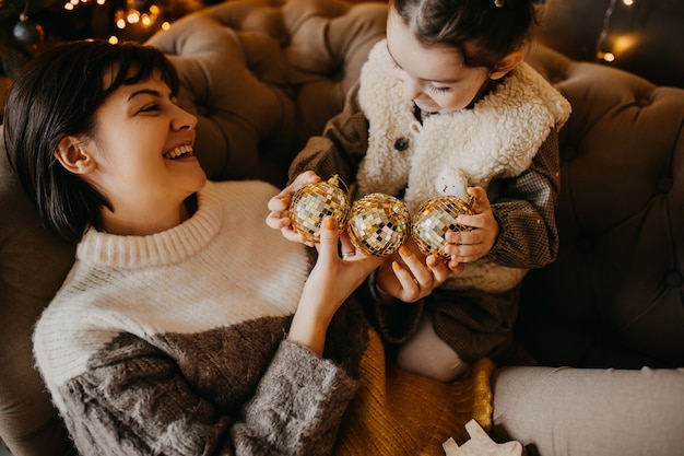 Madre e hija jugando con bolas de árbol de Navidad en casa