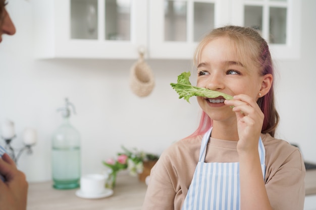 Madre e hija jugando y divirtiéndose con verduras en la cocina