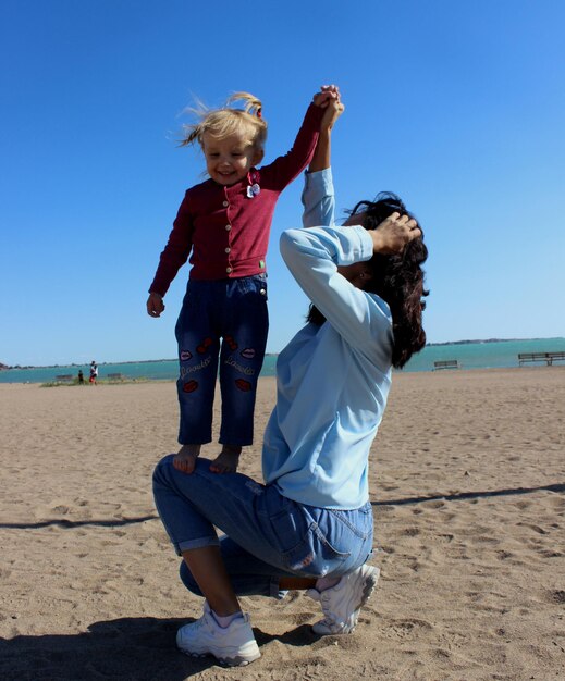 Foto madre e hija jugando en la playa contra un cielo despejado