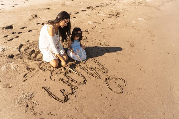 Madre e hija juntas escribiendo "Te amo mamá" en la arena de una playa