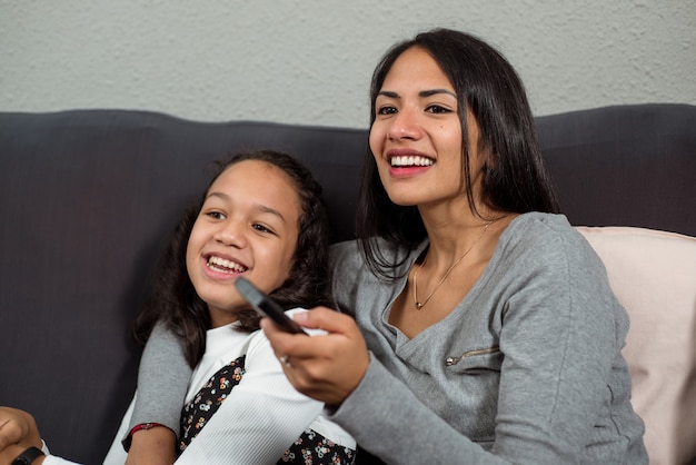Madre e hija latinas riendo viendo series en la televisión.