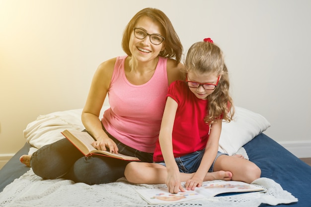 Madre e hija leen libros en casa en la cama.