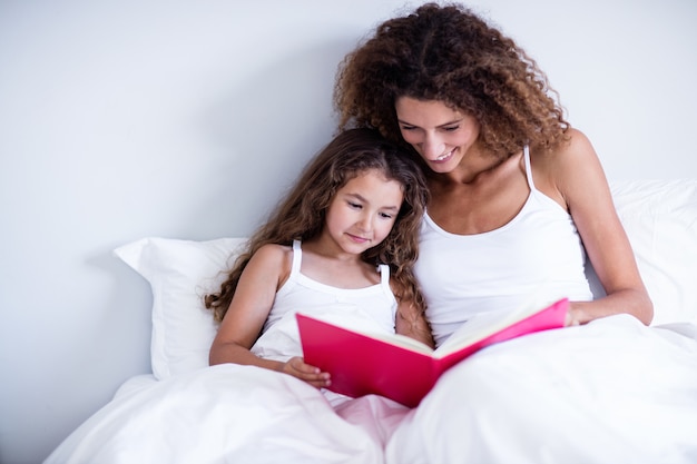 Madre e hija leyendo un libro juntos en la cama