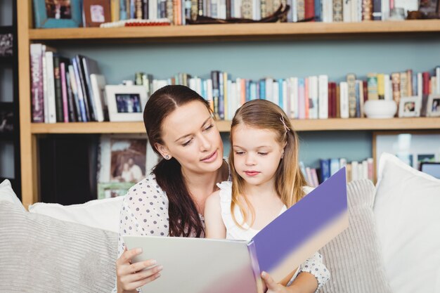 Madre e hija leyendo un libro en el sofá en casa