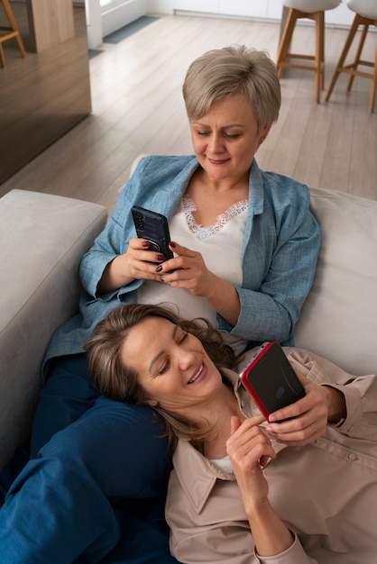 Foto madre e hija leyendo mensajes en teléfonos inteligentes juntos en casa en el sofá