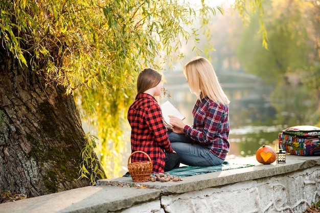 Madre e hija leyendo y relajándose cerca del lago