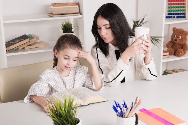 Madre e hija leyendo sentados en casa a la mesa.