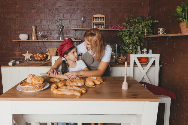 Madre e hija linda están preparando la masa para hacer un pastel en la cocina de casa. Día de la Madre.