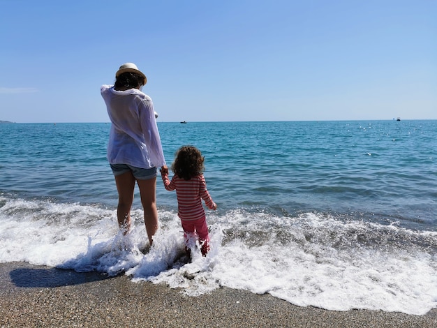 Madre e hija de la mano con los pies descalzos frente a la playa