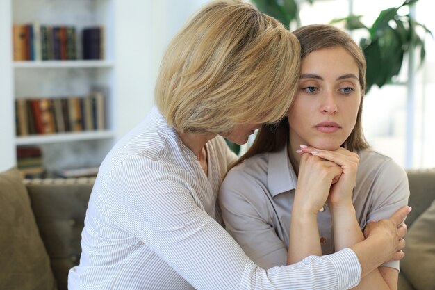 Madre e hija de mediana edad hablando en el sofá en la sala de estar.