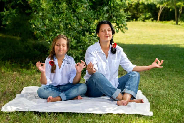 Madre e hija meditando sentadas en el pasto