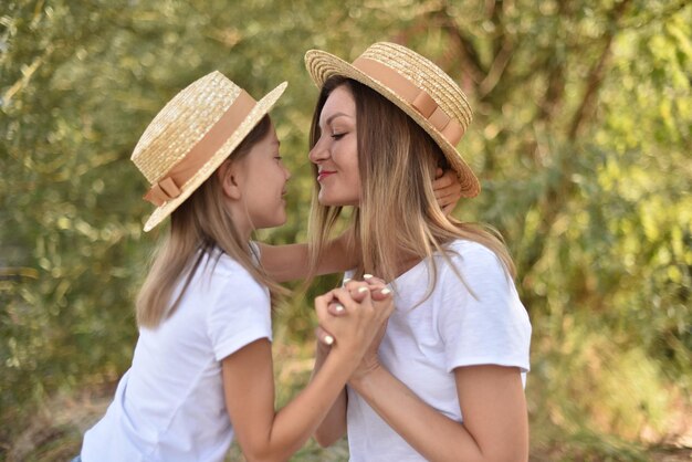 Madre e hija se miran amorosamente en el fondo del árbol verde en el parque familiar de vacaciones