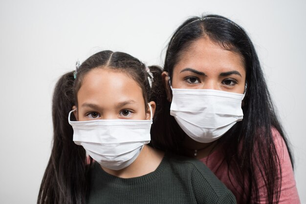 Madre e hija mirando a la cámara usan una máscara médica