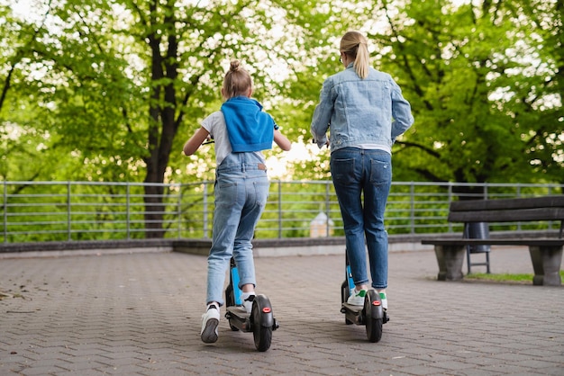 Madre e hija montando scooters eléctricos en el parque de la ciudad