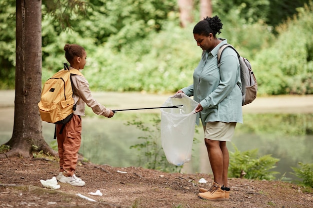Madre e hija negras ayudando a limpiar la naturaleza juntas y recogiendo basura