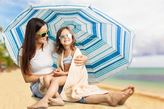 Madre e hija bajo el paraguas de la playa poniéndose crema solar