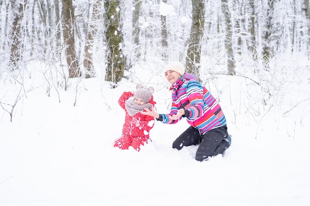 Madre e hija en paseo invernal en la naturaleza. mujer y niño niña hacen muñeco de nieve